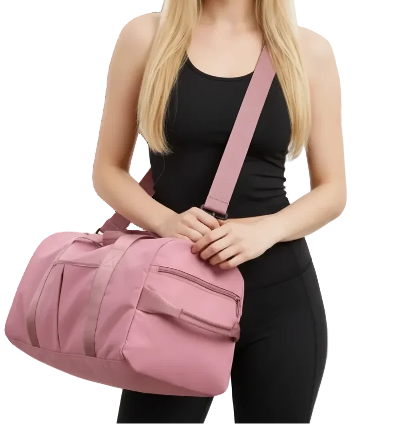 A blonde woman in a black tank top and leggings carries a pink duffel bag with a matching pink shoulder strap against a plain white background.
