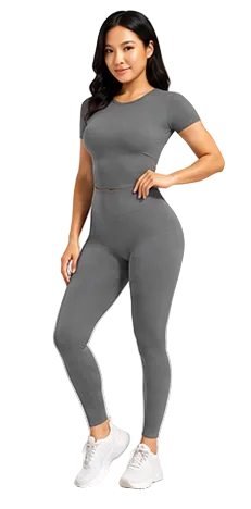 A woman modeling a tight-fitting gray short-sleeve bodysuit and matching leggings set, paired with white sneakers, against a light gray studio background.