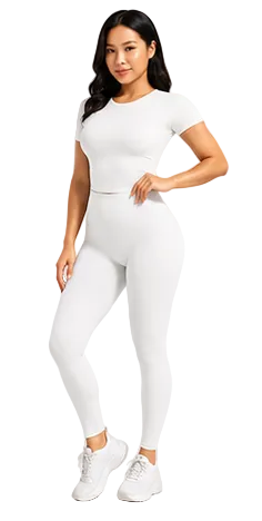 A woman modeling a matching white short-sleeve crop top and high-waisted leggings set, paired with white sneakers, against a light gray studio background.