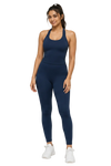 A woman modeling a matching navy blue athletic set consisting of a halter-neck tank top and high-waisted leggings, paired with white sneakers, against a plain white background.