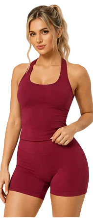 A woman modeling a matching burgundy activewear set consisting of a racerback tank top and high-waisted biker shorts against a plain beige studio background.